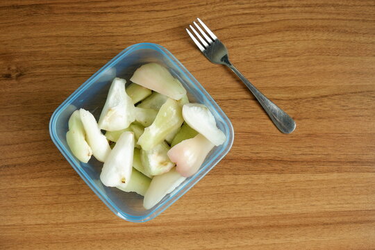 Top view of freshly cut Indonesian wax apples, known as jambu air, in a clear container and a fork on a wooden table, showcasing crisp white, green, and pink fruit pieces.