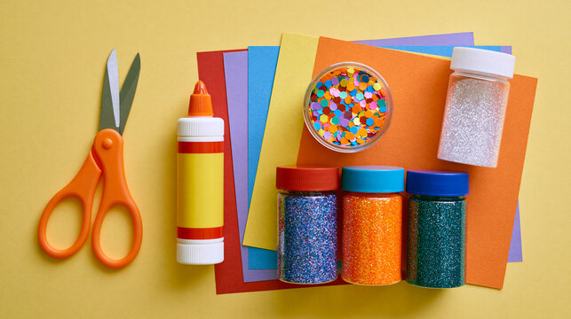 Bright colorful craft supplies featuring scissors and glitter bottles arranged neatly on paper sheets