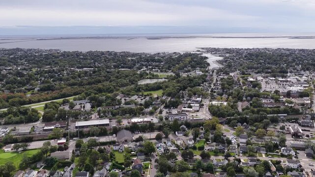 Drone pans over Babylon on Long Island toward Great South Bay in New York. Marinas and waterfront neighborhoods meet calm waterways while parkland and tree lined streets fill the foreground below.