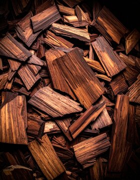 Close-up image of brown wooden chips with varied textures and grain patterns, scattered in a pile against a dark background.