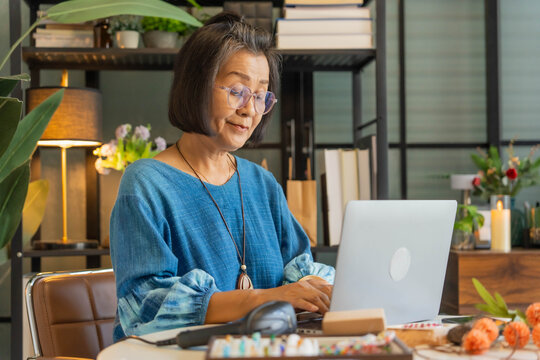 Mature Asian woman typing on laptop manage online store handcrafted jewelry