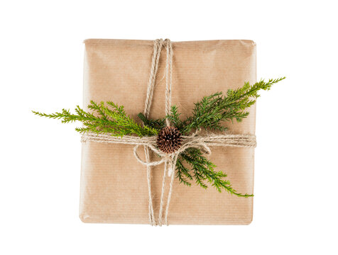 Rustic Christmas gift box wrapped in kraft paper with twine, green cedar branches and small pine cone isolated on transparent background