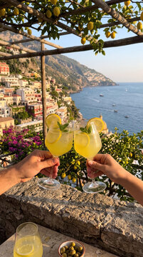 Couple toasting with limoncello spritz cocktails on terrace in Positano Italy