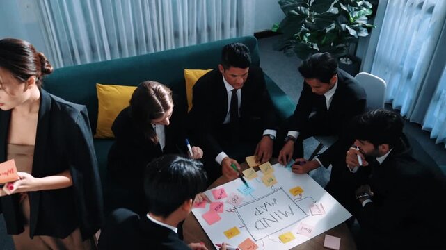 Top view of businesswoman write marketing idea on stick notes while standing near group of diverse people brainstorm financial strategy by using mind map. Start up team working together. Directorate.