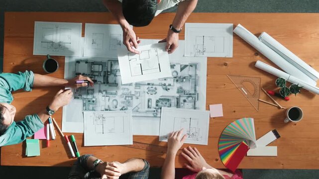 Top view of smart architect engineer team talking about project plan while manager walking at meeting table and start working and analyze building construction and looking at blueprint. Symposium.