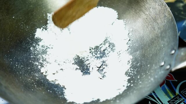 White powder in a metal wok with wooden spatula, Close-up of a metal wok holding a mound of fine white powder, with a wooden spatula above it, suggesting food preparation in a home kitchen.