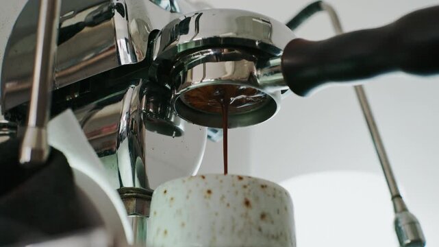 4K Pouring coffee stream from professional machine in cup. Barista man making double espresso, using filter holder. Flowing fresh ground coffee. Drinking roasted black coffee in the morning.	
