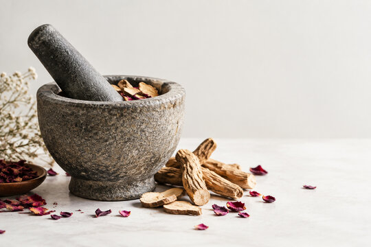 Stone mortar and pestle with dried mandrake roots and petals, herbal apothecary still life