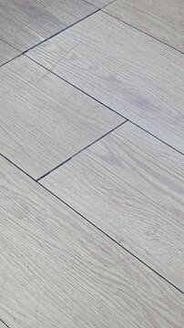 Close-up of light gray wood grain laminate floor covered with cut hair strands and dirt in barber shop, unclean salon flooring with plank gaps