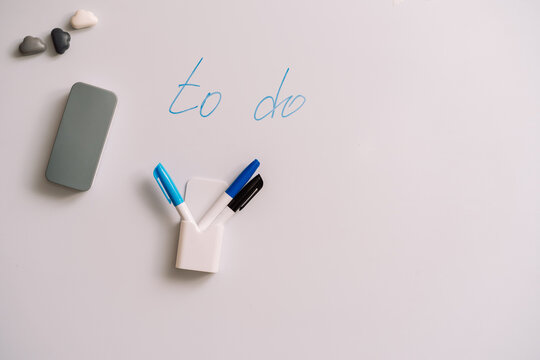 Whiteboard with to do text and three markers in a holder beside a gray eraser.