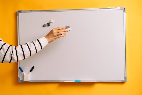 Hand holding an eraser sideways before a blank whiteboard with its edge visible.