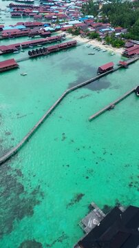Vertical aerial drone view of Derawan Island Berau East Kalimantan - long wooden pier over turquoise coral reef water and fishing village