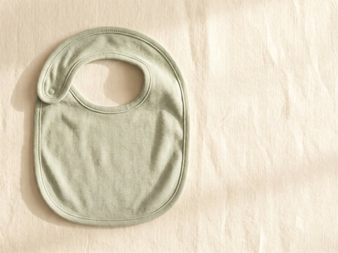 Plain sage green cotton baby bib on a warm cream background
