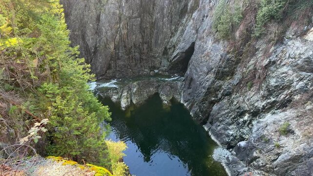 Deep green canyon pool below Cleveland Dam at Capilano River in Vancouver, surrounded by steep rocky cliffs and green forest in a dramatic natural gorge.