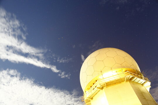 Radar dome glowing under starry night sky.