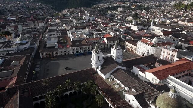Quito, Ecuador. Aerial view of Quito's historic Plaza de San Francisco. Red-tiled roofs contrast with white colonial walls. Two prominent towers stand near the square's center. Drone shot.