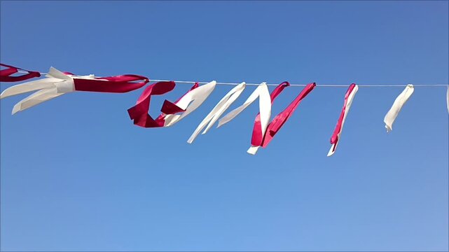 Red and white flags. Red and white Latvian national flag color ribbons fluttering on line against clear blue sky, celebration patriotism concept.