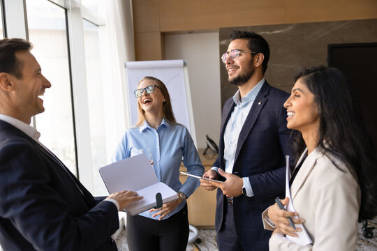 Multiethnic colleagues laughing during informal meeting in office boardroom, having friendly, casual conversation, discussing business project, ideas or presentation results. Communication, teamwork