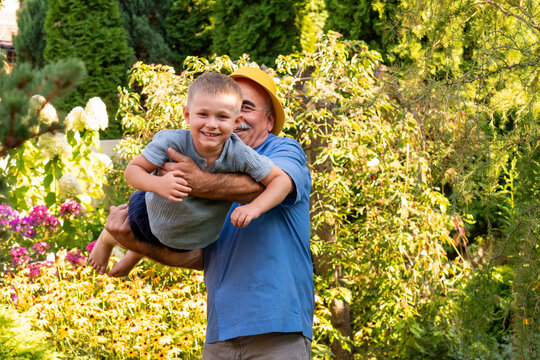 Grandfather Hugging Smiling Grandson During Playful Garden Moment