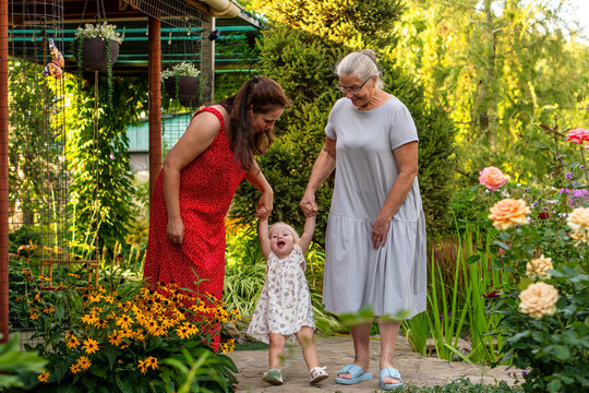 Mother And Grandmother Playing With Little Girl In Garden