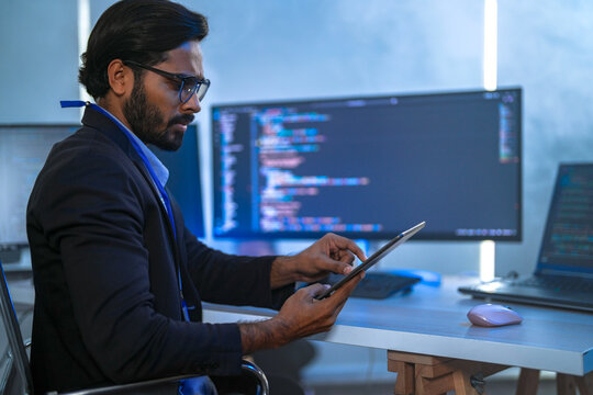 A female software engineer with curly hair and glasses entering commands at the workstation, typing at a keyboard while a colleague watches in a tech office; medium shot of software.