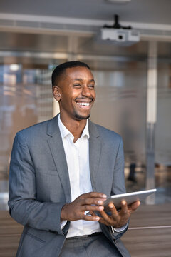 Portrait of laughing African businessman working on corporate task, holding digital tablet in office, representing online workflow, project updates check, positive news or business information review
