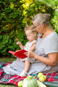 Grandmother Sharing Red Storybook With Granddaughter on Picnic Blanket