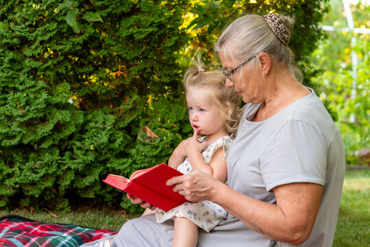 Thoughtful Granddaughter Reading Book With Grandmother in Summer Garden
