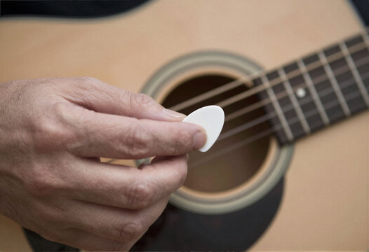 A hand using a guitar pick to strum a string, macro