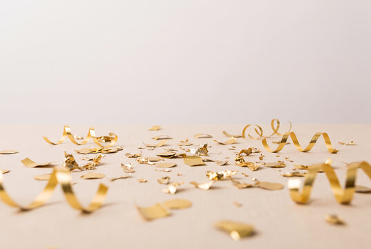 Gold confetti and ribbon scattered on beige background celebration