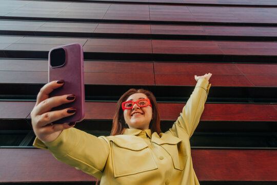 Redhead white woman in yellow shirt and bright glasses taking selfie with phone