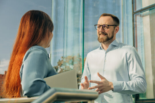 Businessman and businesswoman discussing project in office with glass doors, sunny day