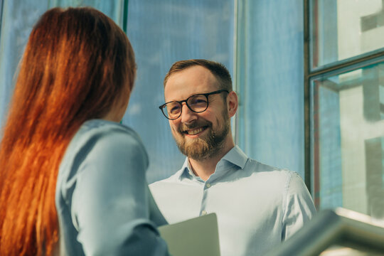 Businessman and businesswoman discussing project in office with glass doors, sunny day