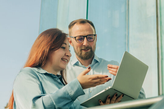 Businessman and businesswoman discussing project in office with glass doors, sunny day