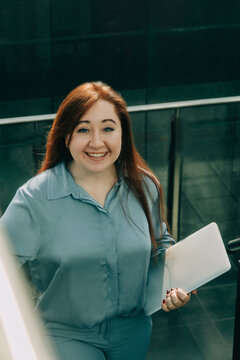 Redhead businesswoman in blue suit with laptop walking up office stairs