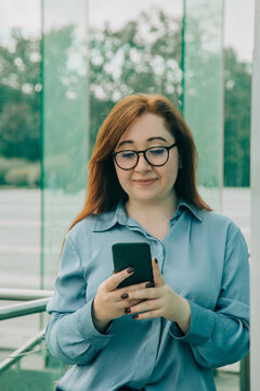 Redhead businesswoman in blue suit using phone app, glasses, looking at display