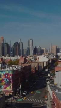 Vertical video: Backwards reveal of buildings along street in urban borough. Tall downtown skyscrapers in distance. Brooklyn, New York City, USA