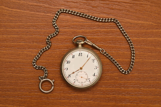 Vintage pocket watch with a chain on a vintage brown wooden table. Top view. Authentic vintage objects and nostalgia concept.