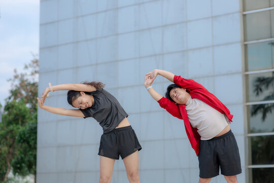 Asian fitness trainer coaching sporty woman doing side bend warmup stretching in park. Active healthy couple lifestyle, outdoor workout training and wellness exercise concept.