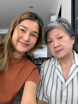Happy Asian Mother and Daughter Taking a Selfie Together Indoors, Sharing a Joyful Moment