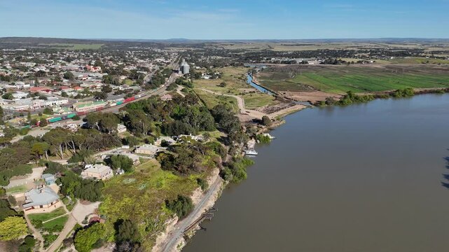 Aerial drone view over Murray Bridge in South Australia. A long intermodal freight train carrying shipping containers passing through the regional township,&nbsp;and wide Murray River