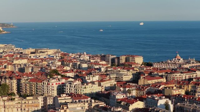 Slow telephoto sideways move over red rooftops toward Baie des Anges with a cruise ship and yachts, golden hour, Nice, French Riviera, Cote d Azur, France