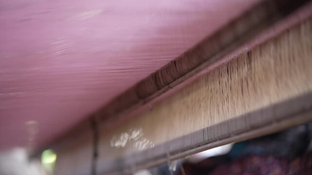 Close up of fine pink silk threads moving through the heddles on a traditional weaving loom.