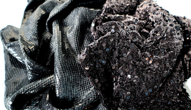 A close view of textiles in black colors is shown. One fabric has a smooth finish, and the other has shiny sequins. These materials are often used in clothing and home decor.