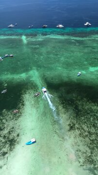 Vertical drone orbits and pans up while tracking a boat departing Doljo Beach across reef waters in Panglao, Bohol, Philippines