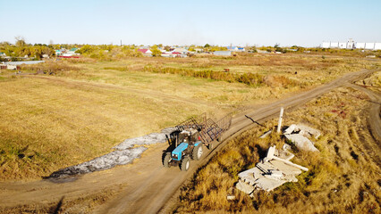 Aerial View of Blue Farm Tractor Towing Cage Trailer on Rural Dirt Road © Andrey