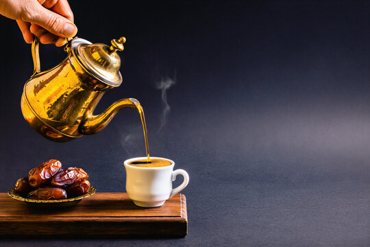 Brass dallah pouring golden Arabic coffee into a small cup