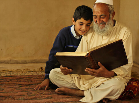 Grandfather and grandson reading a book together by lamplight