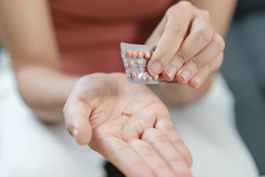 Close up woman holding oral contraceptive birth control pills blister pack and a glass of water, concept of unwanted pregnancy prevention and female healthcare.
