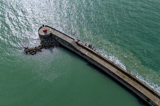 High-angle aerial view of the concrete pier and breakwater structure extending into the green waters of the English Channel in Newhaven, East Sussex, England